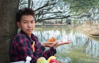 Young asian boy in plaid shirt sitting by the pond in the backyard and spending his free time by drawing, coloring and fixing his fruit and animal models sculpted from plaster with watercolor happily.