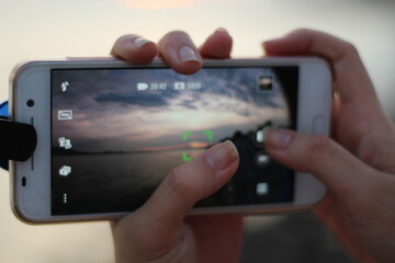 hands hold phone to take sunset photo︱focusing and light setting tips