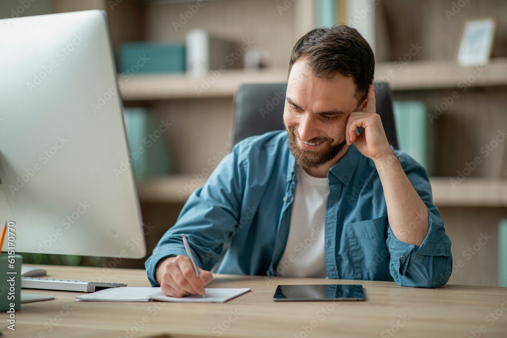 Poster handsome businessman talking on cellphone and taking notes while working in office