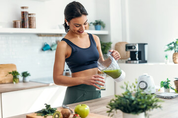 Athletic woman preparing smothie while listening music with earphones in the kitchen at home.