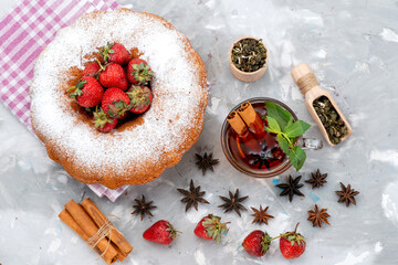a top view round cake with sugar powder red strawberries cinnamon tea on the white desk berry fruit cake sweets
