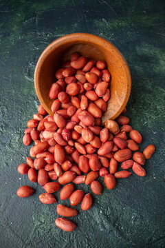 Close up view of red peanuts fallen from brown pot on blue and black background