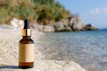 Dropper bottle on a stone, exotic beach backdrop. Natural cosmetic concept.