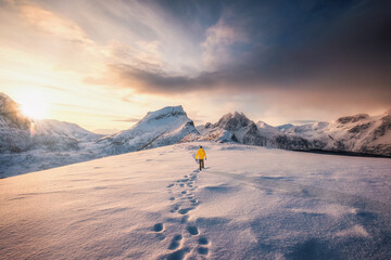 Mountaineer walking with footprint in snow storm and sunrise over snowy mountain in Senja Island © Mumemories