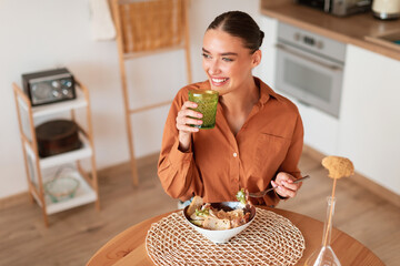 Flavors of freshness. Young woman drinking a glass of water while savoring a caesar salad at home, above view