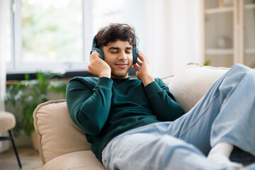 Relaxed Guy Pressing Headphones To Ears Listening Music At Home