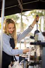 Female barrista making coffee for clients in a mobile coffee stand outdoors in a city