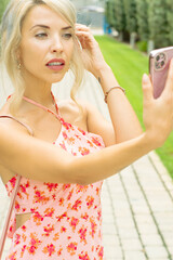 PRETTY GIRL SMILING WHILE IS TAKING A SELFIE AND CALLING BY PHONE IN THE STREET