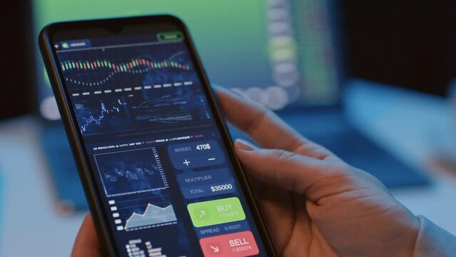 Tilt close up of unrecognizable person holding smartphone with analytical crypto app on indoor at night time