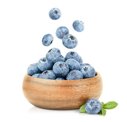 blueberries in a wooden plate and berries falling into it on a white isolated background
