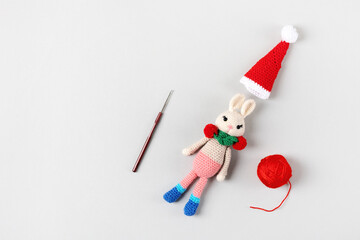 Fototapeta na wymiar Knitted toy bunny in a red hat and scarf with ball of thread and knitting hook on gray background. Baby stuff and accessories. Gift for winter holidays. Top view, flat lay.