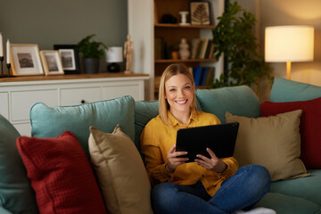 Obraz premium Relaxed woman sitting on sofa using digital tablet at home