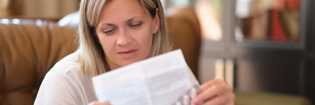 Young woman holds package of pills and reads medical instructions