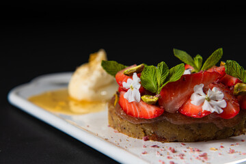focus on a Gastronomic delights of restaurant dishes, strawberry pie  dessert with ice cream on a white rectangular plate isolated on a black background, culinary arts