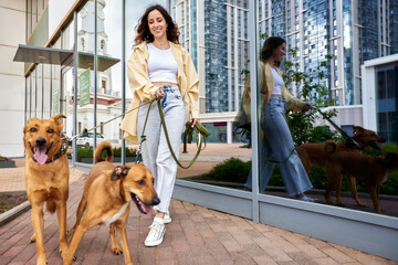 Charming young smiling girl on a walk with two golden dogs in the city yard. The girl keeps pets on a leash. Love and affection between owner and pet. Adopting a pet from a shelter.