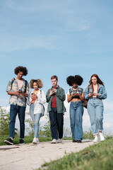 Group of university students walking around the campus looking at their mobile phones. Concept: technology, addiction, youth