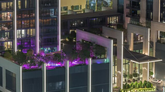 Luxury swimming pool on roof top during amazing evening aerial timelapse. Illuminated colorful water with palms and trees. Vacation and holidays concept. Glowing windows of skyscraper. Dubai, UAE