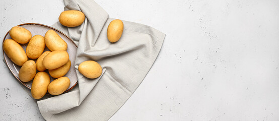 Plate with raw potatoes on light background with space for text