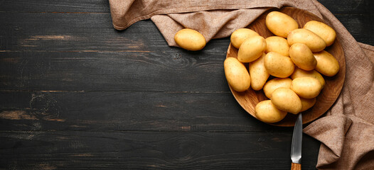 Plate with raw potatoes and knife on dark wooden background with space for text