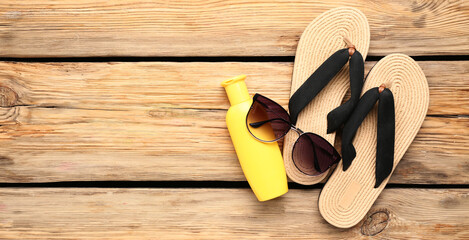 Sunscreen cream, sunglasses and flip-flops on wooden background with space for text