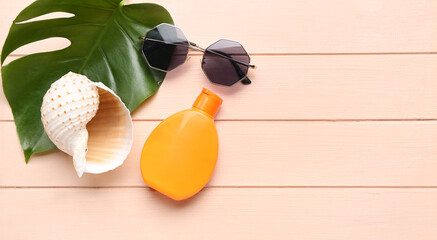 Sea shell, sunscreen cream, tropical leaf and sunglasses on wooden background with space for text