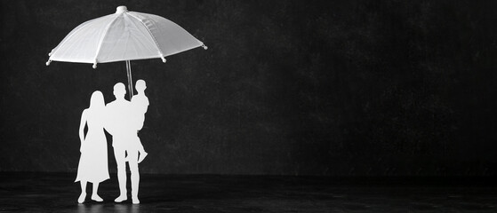 Small umbrella and paper figure of family on black background with space for text