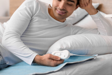 Young man lying on electric heating pad in bedroom, closeup © Pixel-Shot