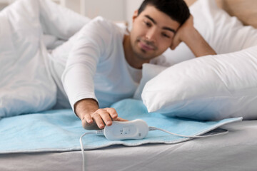 Young man lying on electric heating pad in bedroom, closeup © Pixel-Shot
