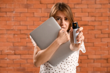 Young woman with laptop and pepper spray for self-defence on brick background