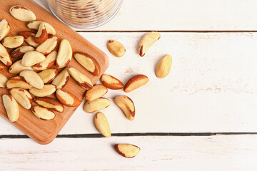 Cutting board with tasty Brazil nuts on light wooden background