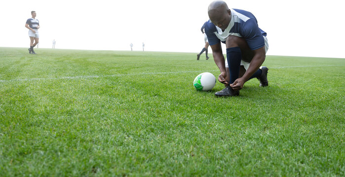 Digital png photo of african american rugby player tying shoe on transparent background - Powered by Adobe