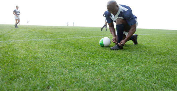 Digital png photo of african american rugby player tying shoe on transparent background - Powered by Adobe