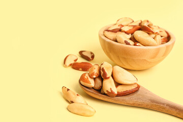 Wooden bowl and spoon with tasty Brazil nuts on yellow background