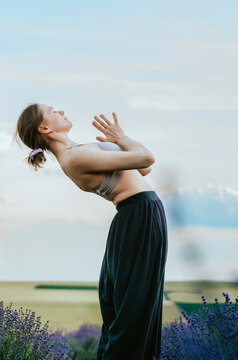 Woman in palazzo pants and top doing yoga backbend with namaste hands in rural lavender field