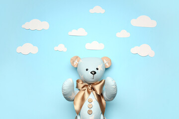 Toy bear with paper clouds on blue background