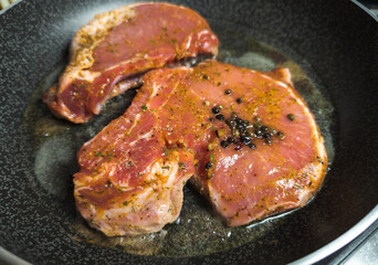 Delicious juicy pork steak seasoned with rosemary and garlic is fried in a pan.
