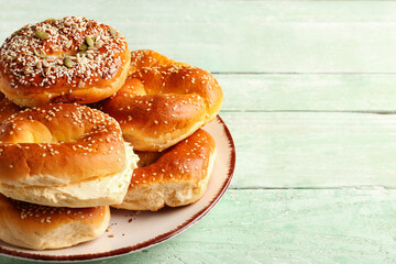 Plate of tasty bagels with sesame and cream cheese on green wooden background, closeup