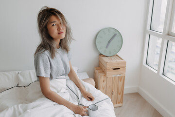 Asian woman just wake up by the clock at 7 AM on the bed in the morning.