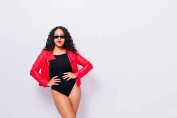 African American curvy female in black bodysuit and jacket on red and white background in studio
