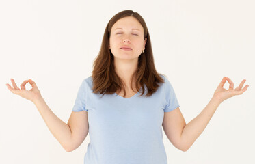 Mindful caucasian pregnant woman meditates indoor, keeps hands in mudra gesture, has eyes closed, tries to relax after long hours of working, holds fingers in yoga sign, isolated on white wall