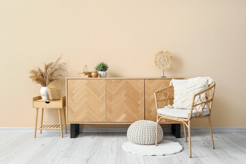Stylish wooden cabinet and comfortable armchair near beige wall