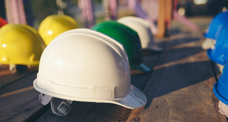 Safety helmet (hard hat) for engineer, safety officer, or architect, place on wooden floor. Yellow, White, green, blue, and orange safety hat (helmet) on construction site-banner  image. - obrazy, fototapety, plakaty