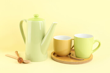 Teapot and tray with mugs on yellow background
