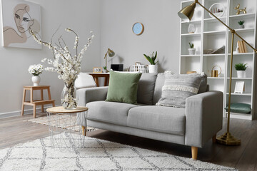 Interior of living room with grey sofa and blossoming tree branches on coffee table