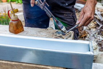 roofer welding stainless gutter with an copper soldering iron. Closeup hand soldering zinc gutter roof. artisan applying weld into the gutter parts to assemble it with tin. 