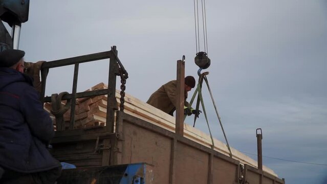 Men unload crane with wood. Clip. Workers unloading wood with crane. Crane with wooden beams is lowered into truck with worker