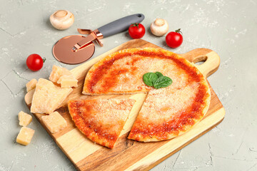 Wooden board of tasty pizza with parmesan cheese, basil and cutter on grey background