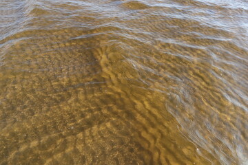 Beautiful background with transparent water and ripples on sandy bottom. Sea waves and gritty surface texture created a pattern of dunes on sand of seabed.