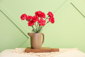 Vase with red carnations on white wooden table near light green wall