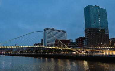 Nervion river with a modernist bridge over it with modern buildings in the background at nightfall Bilbao, Basque Country, Spain